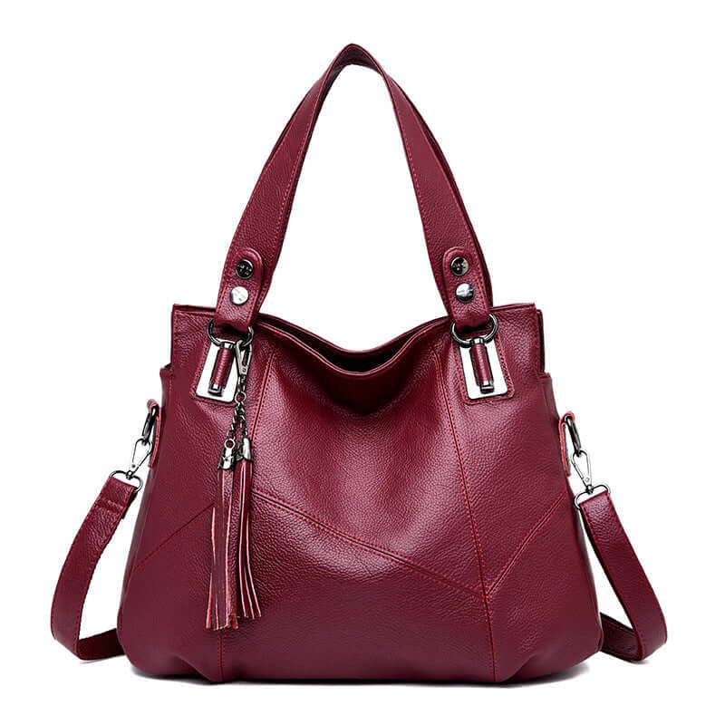 Fashionable large leather shoulder bag for women in deep burgundy color with stylish tassels and dual handles.