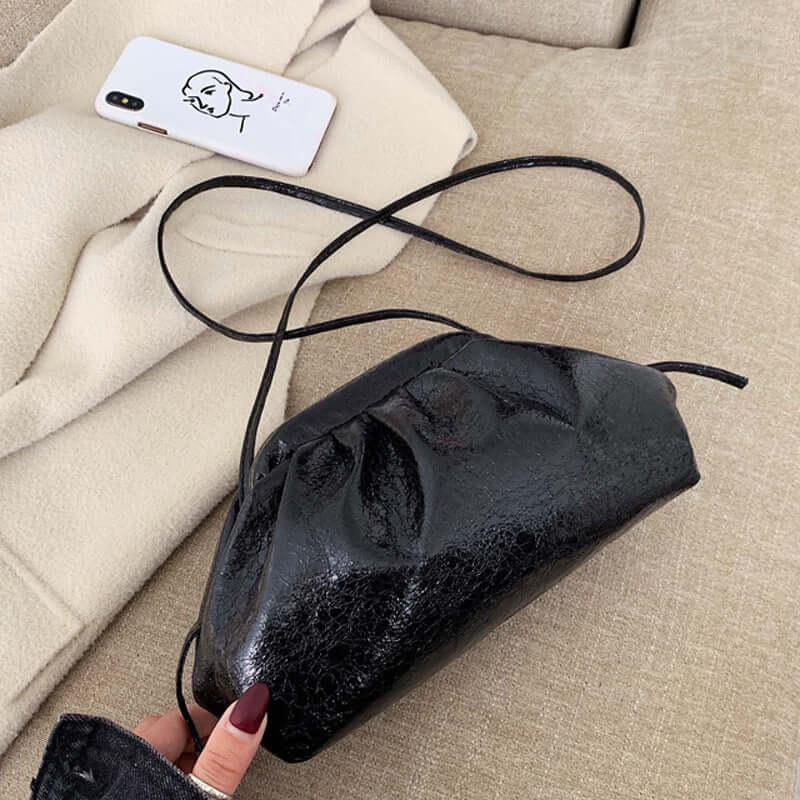 fashion shoulder dumpling bag positioned beside a smartphone on a cozy beige surface.