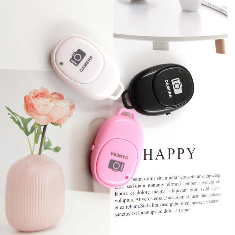 Multifunctional bluetooth remote for selfies in black, white, and pink colors with camera icons.