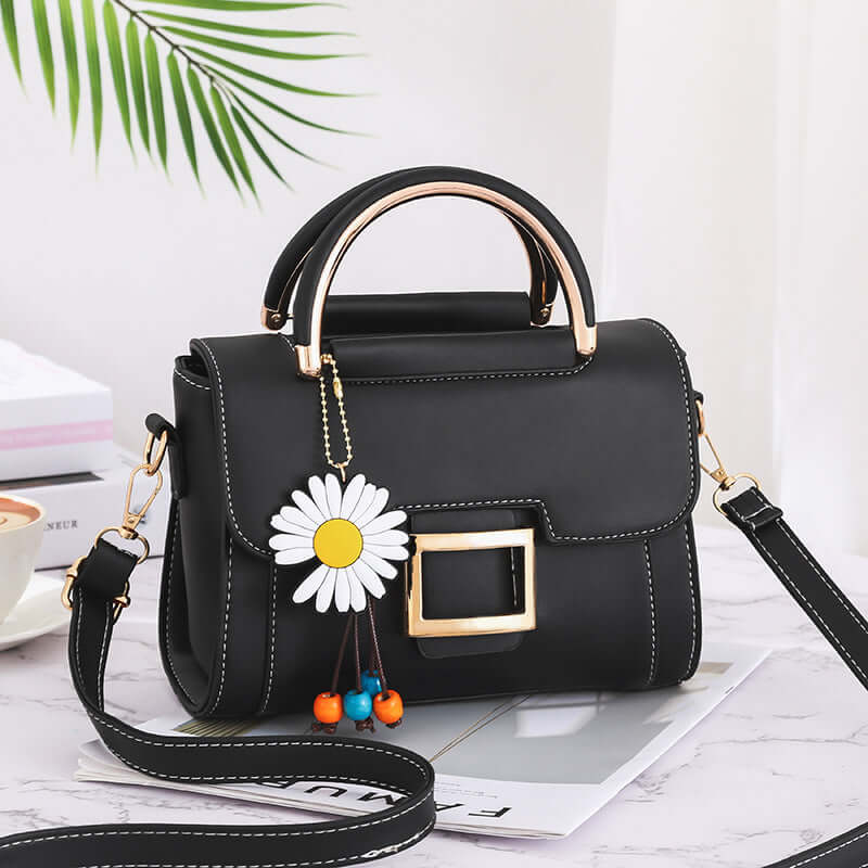 Stylish women's crossbody bag in black with floral charm on table surrounded by stylish decor.