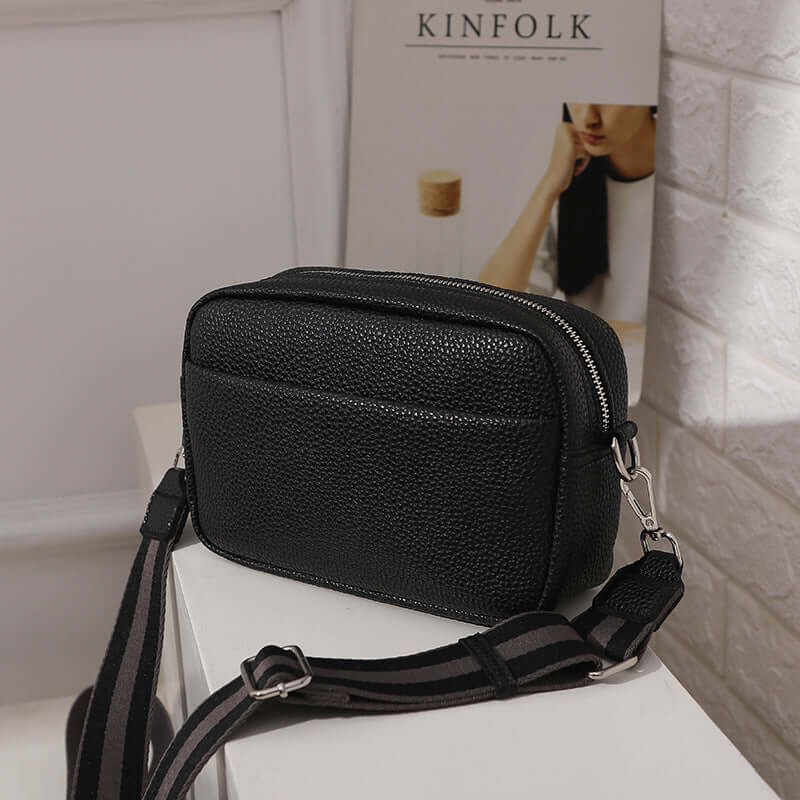 Solid Color Women's Messenger Bag with Wide Strap in black displayed on a table next to a magazine.