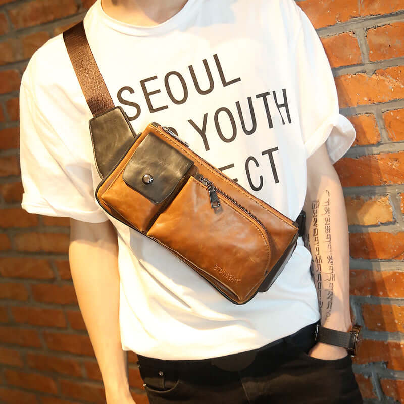 Person wearing a single-shoulder chest bag in brown and black design against a brick wall, showcasing trendy style.