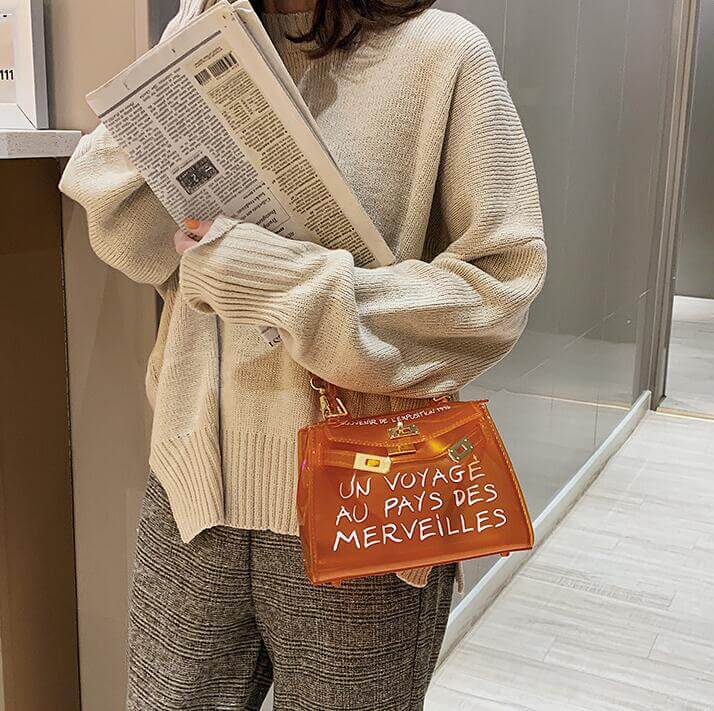 Woman in a cozy sweater holding a jelly shoulder bag with playful text design and newspaper.