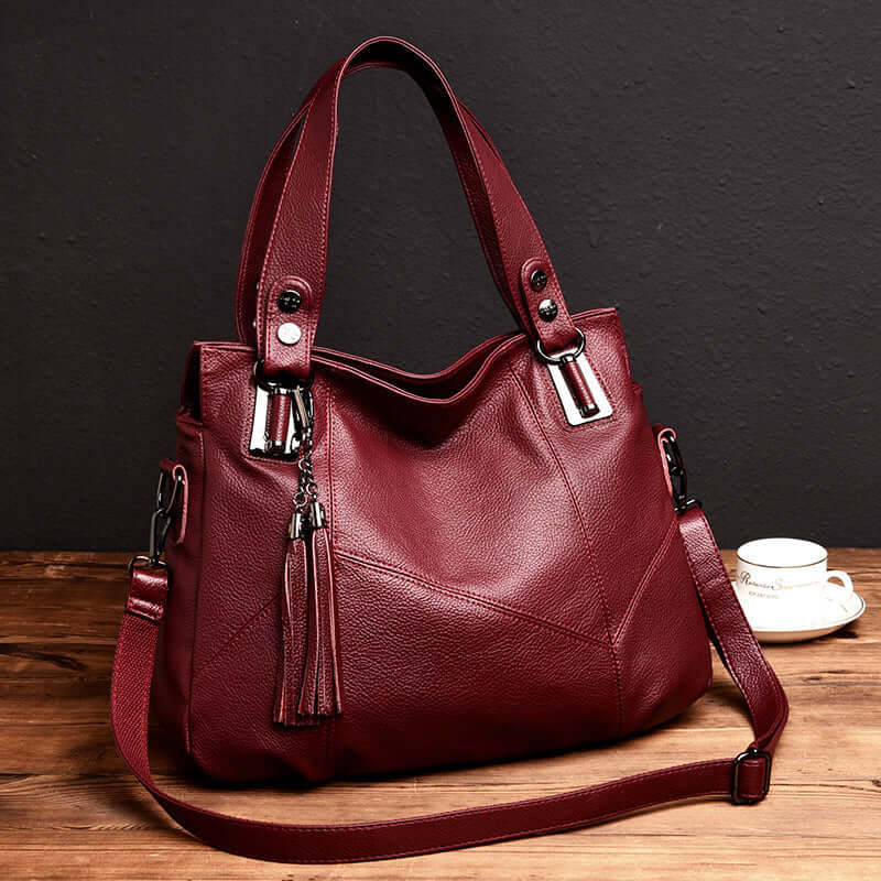 Fashionable large leather shoulder bag for women in burgundy with stylish tassel details.
