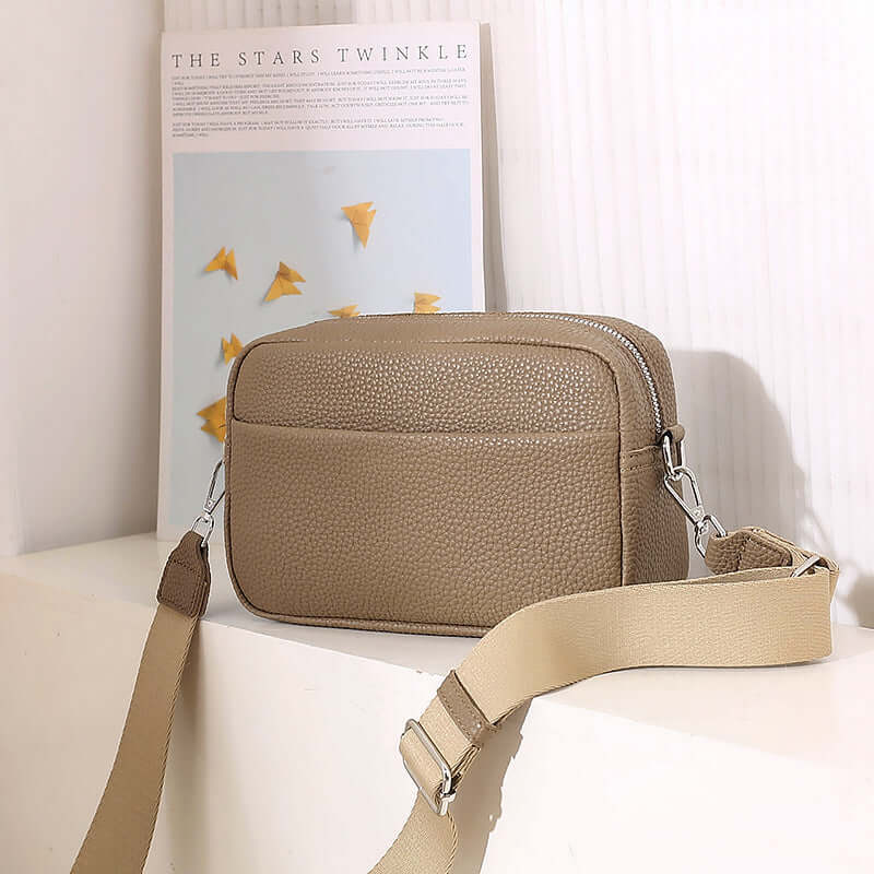 Solid Color Women's Messenger Bag with Wide Strap on a surface next to a decorative poster.