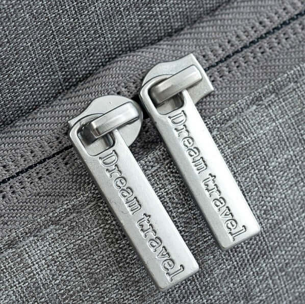 Zipper pulls with 'Dream travel' engraving on a stylish gray travel bag.