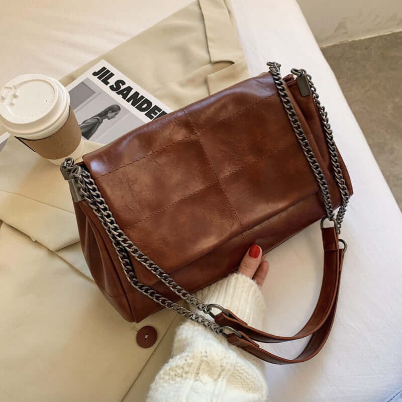 trendy PU leather small square bag in brown with chain strap beside coffee cup and magazine
