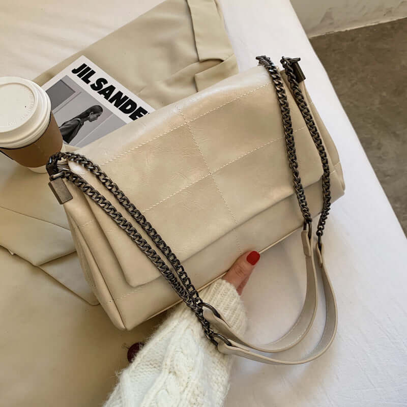 Fashionable PU Leather Small Square Bag for Women in beige with chain strap, styled with coffee and magazine on a table.